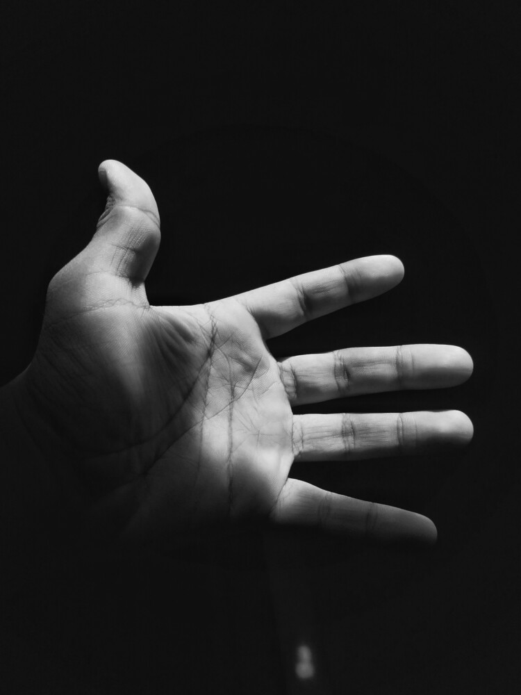 Open hand reaching upward against black background, high contrast black and white studio portrait