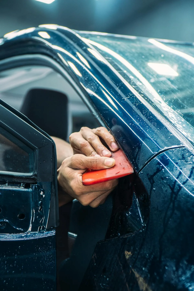 Hand holding red microfiber cloth against wet car hood in daylight