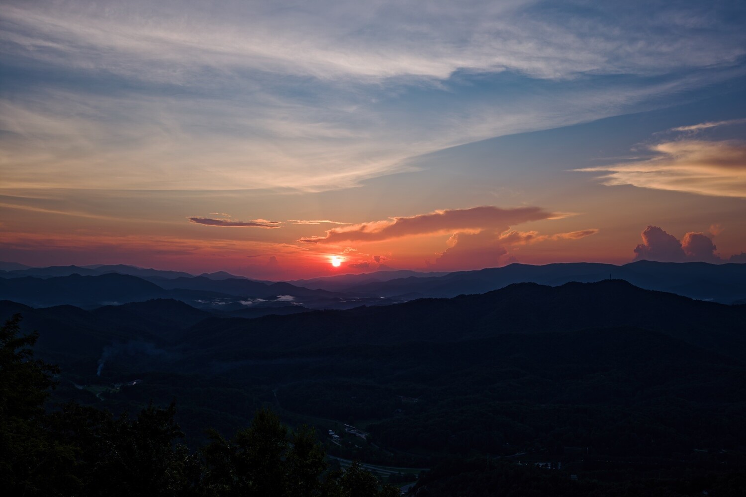 Sunset over layered mountain silhouettes with warm orange and purple sky