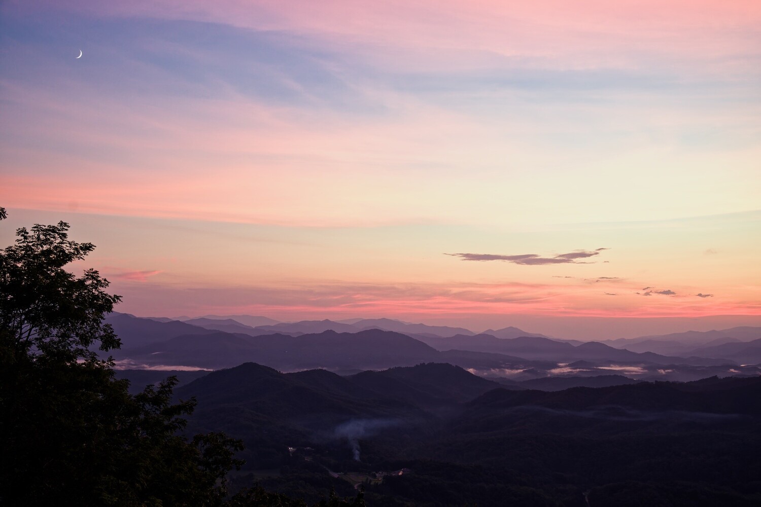 Layered mountain silhouettes at sunset with pink and orange sky