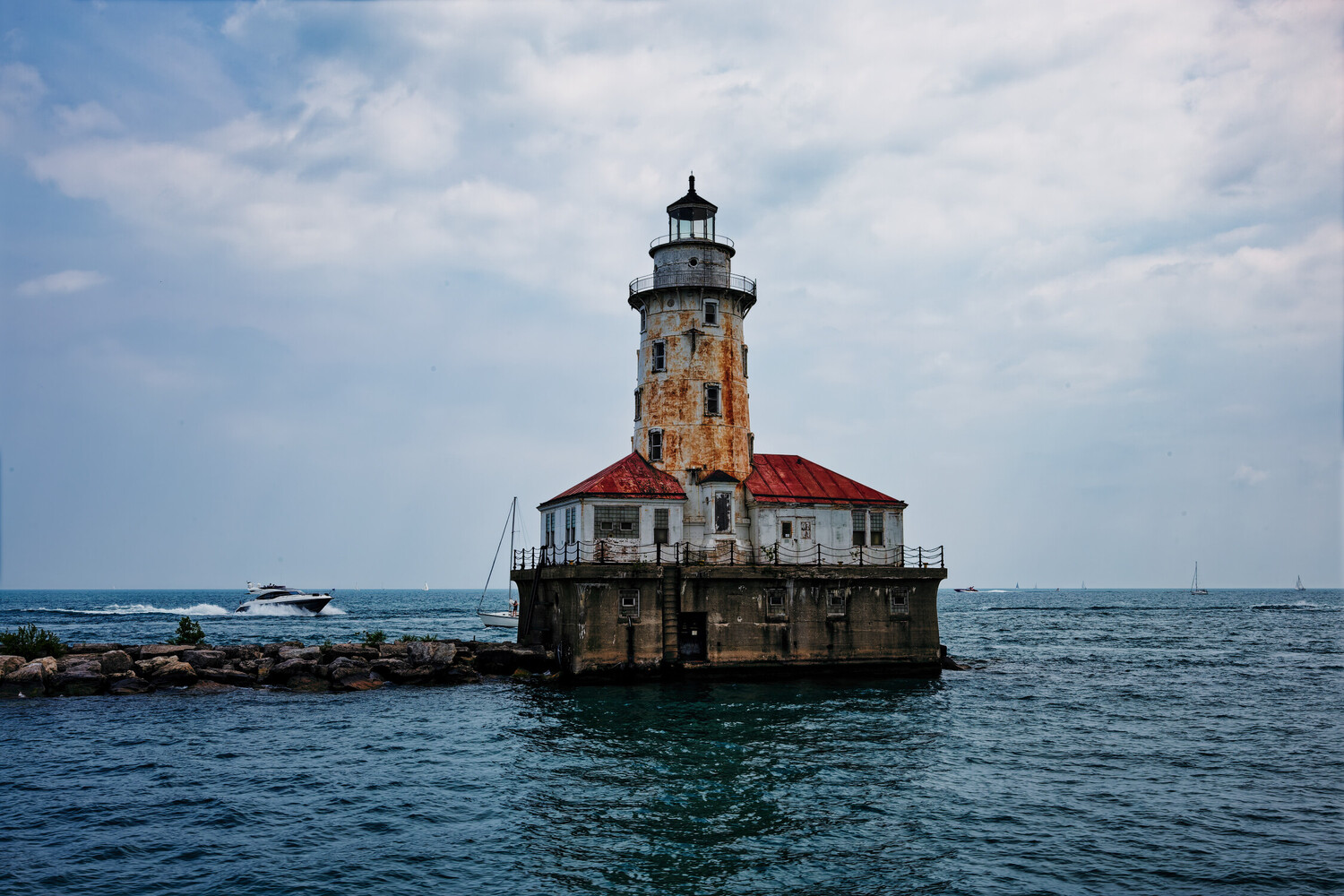 Abandoned lighthouse with red roof on rocky breakwater surrounded by blue water