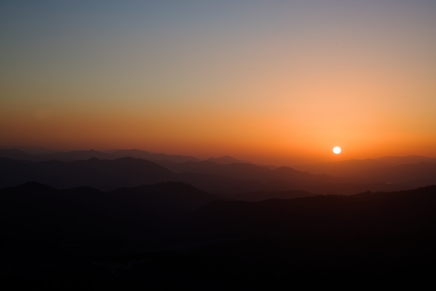 Sun setting over layered mountain silhouettes during golden hour