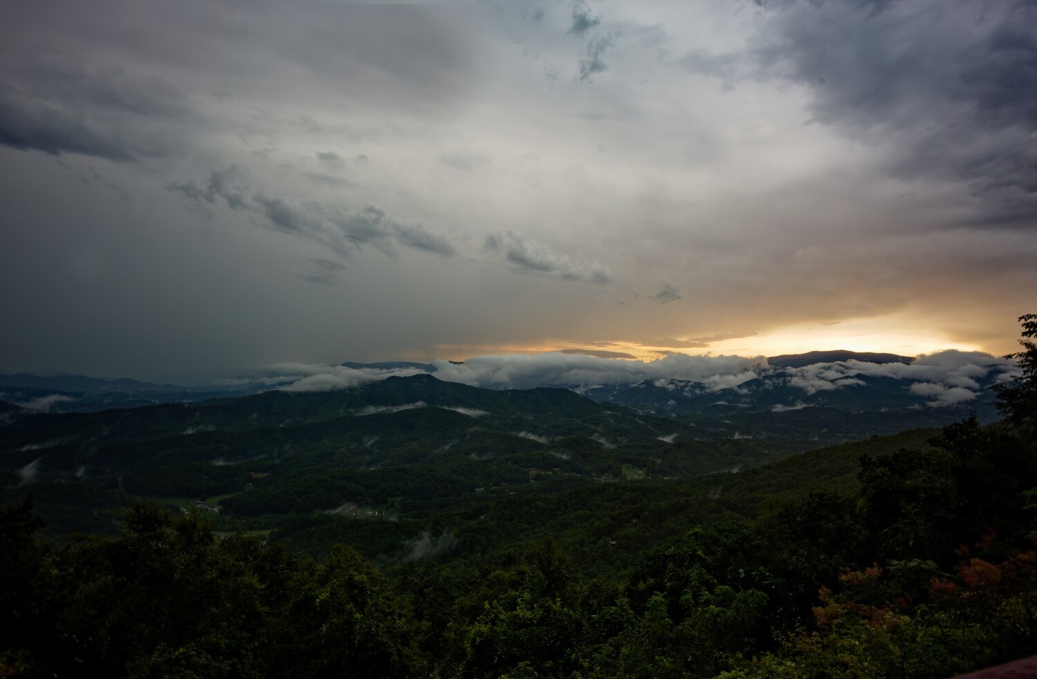 Dramatic mountain valley landscape at sunset with storm clouds and golden light breaking through
