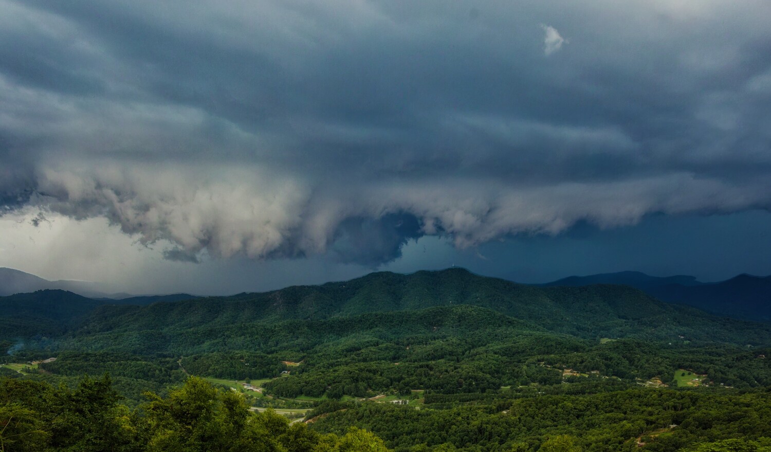 Lush green valley with forested mountains beneath dramatic storm clouds
