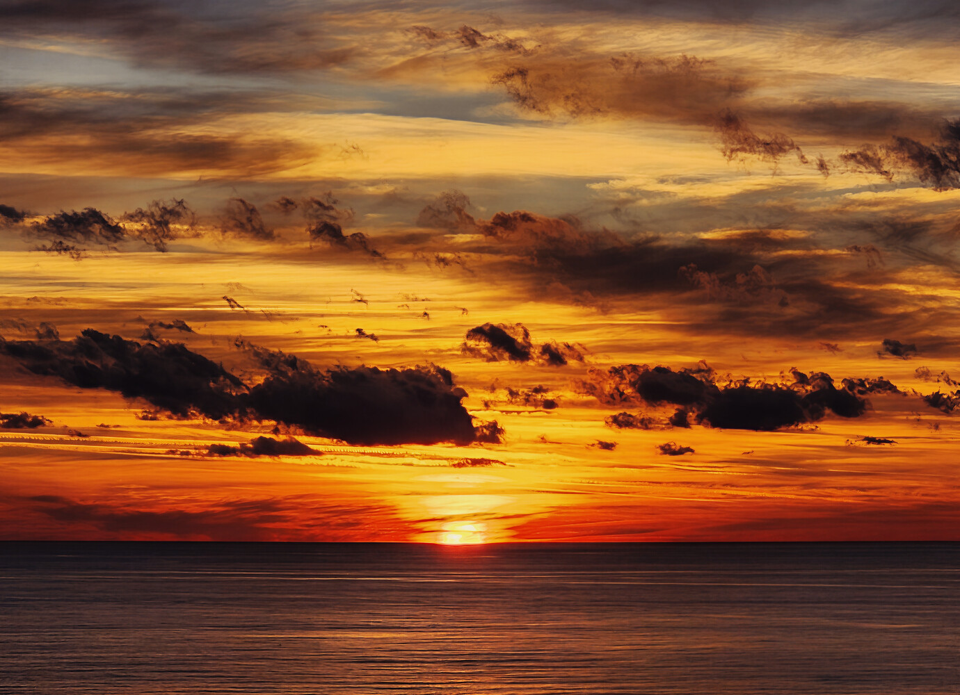 Dramatic golden and orange sunset over calm ocean with layered clouds