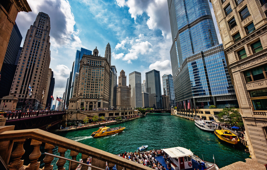 Chicago River with turquoise water, yellow water taxis, and downtown skyscrapers viewed from a bridge