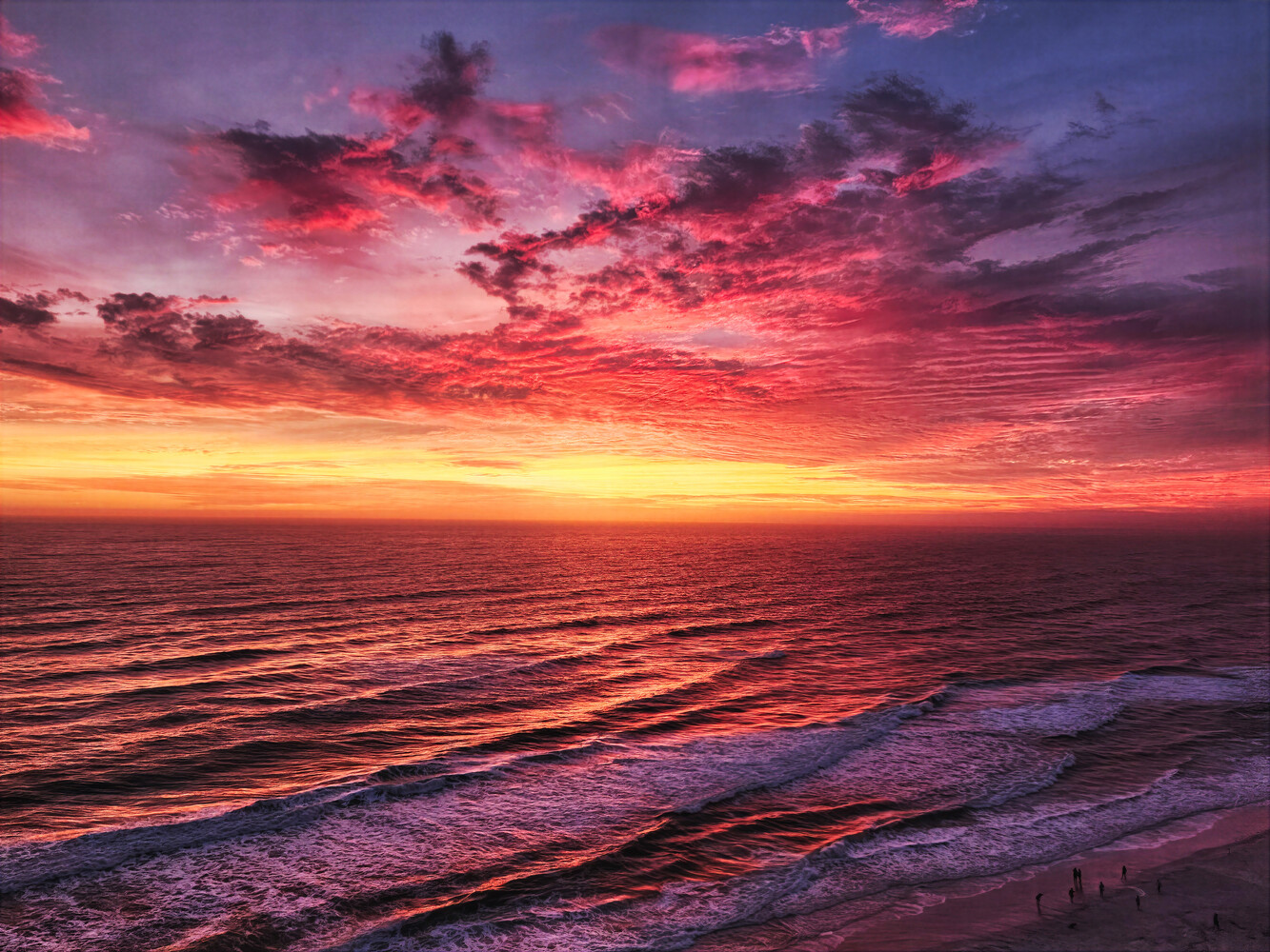 Dramatic sunset over ocean with vibrant pink and purple clouds reflected in wet sand