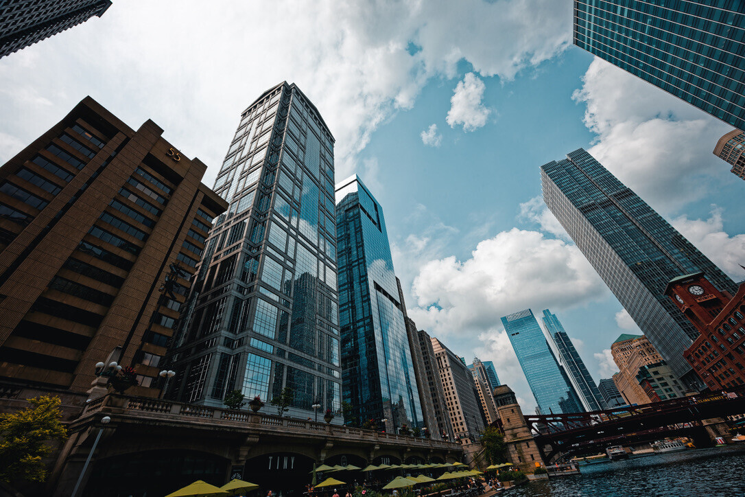 Modern glass and steel skyscrapers line a Chicago River waterway under blue sky with white clouds
