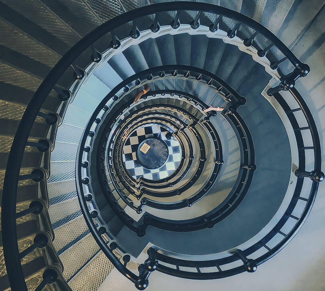 Overhead view of a spiral staircase descending through multiple floors with alternating light and dark steps