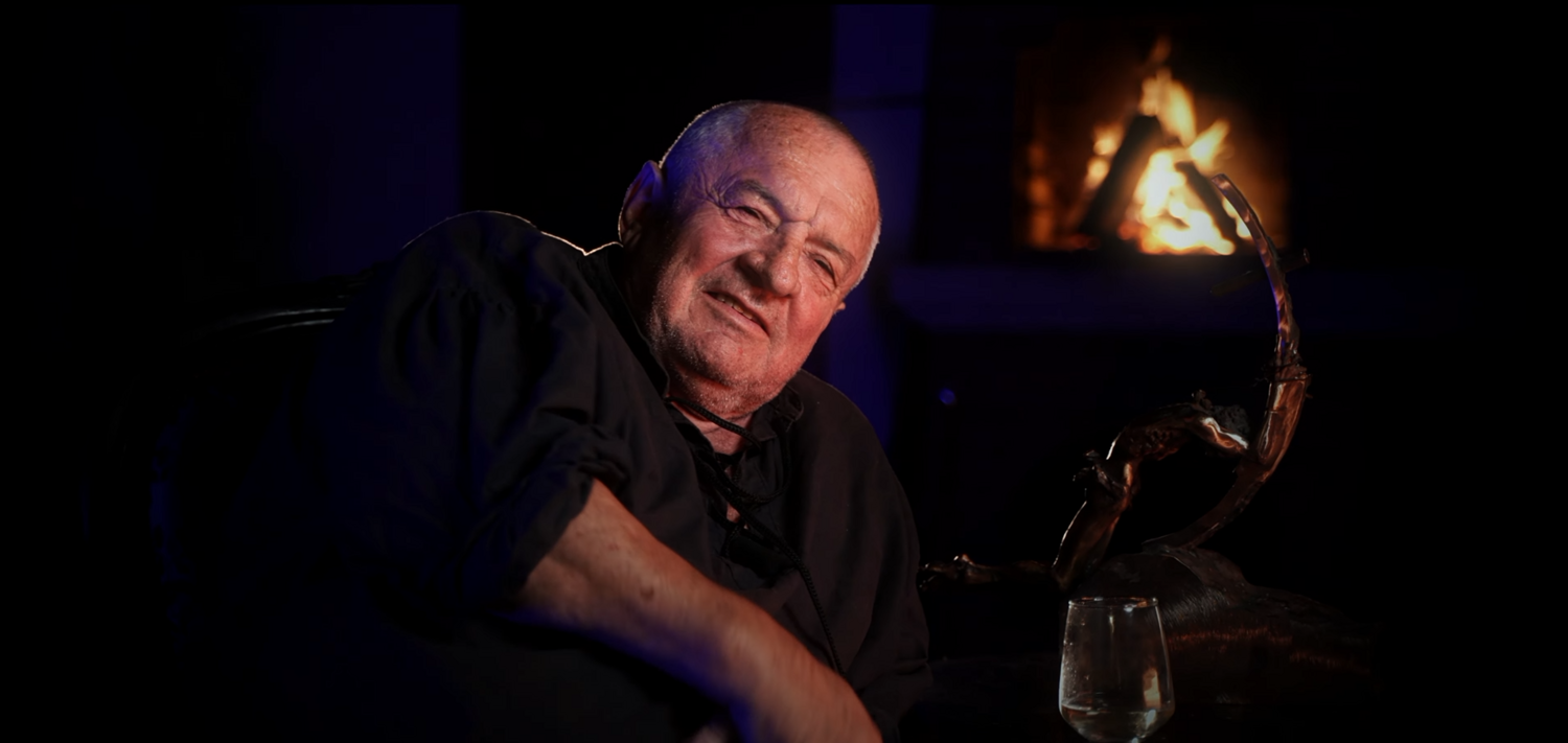 Bald man in black shirt smiling at camera with warm studio lighting and blurred background