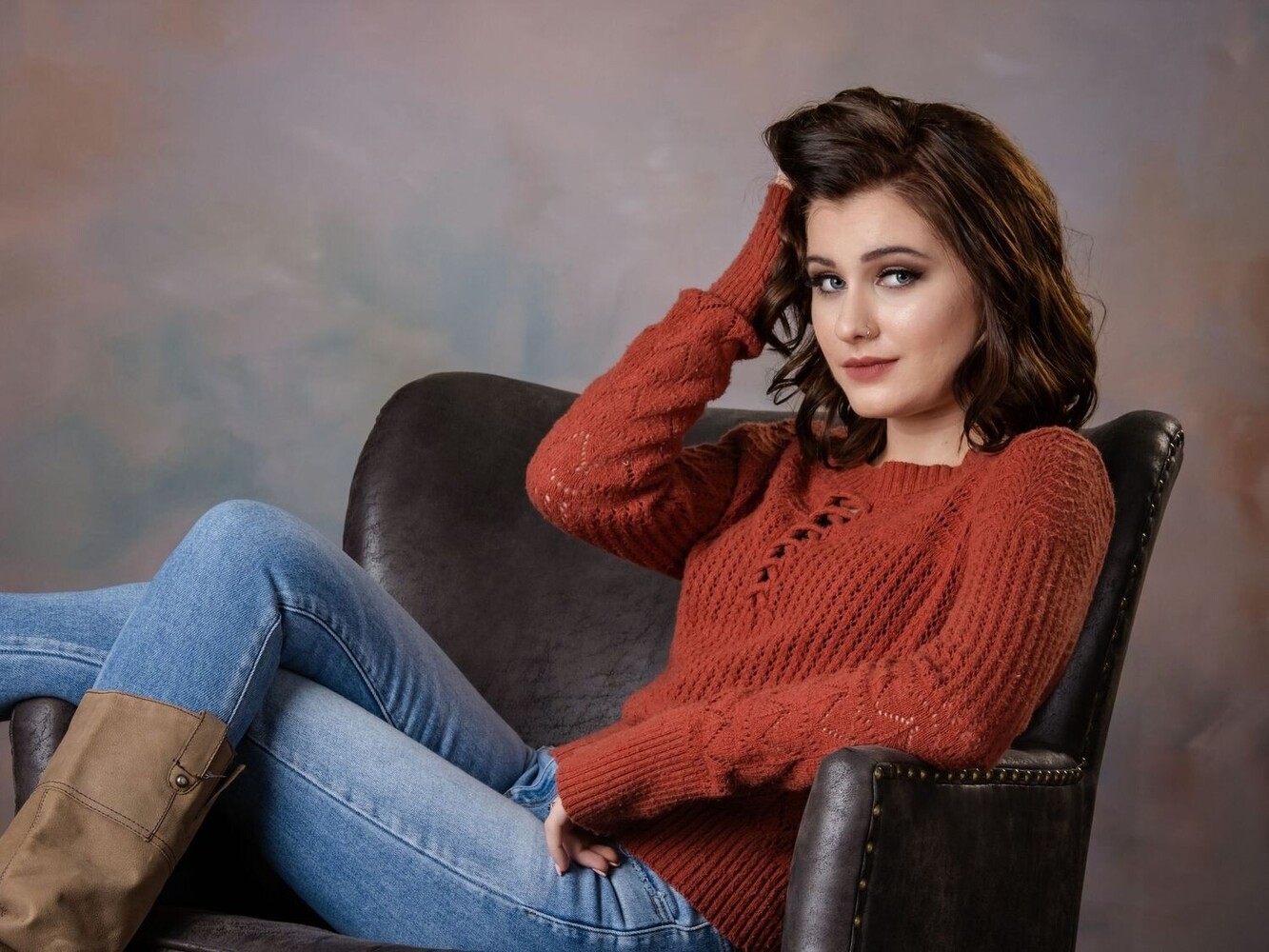 Woman in rust-colored sweater and jeans sitting in black leather chair against blurred background