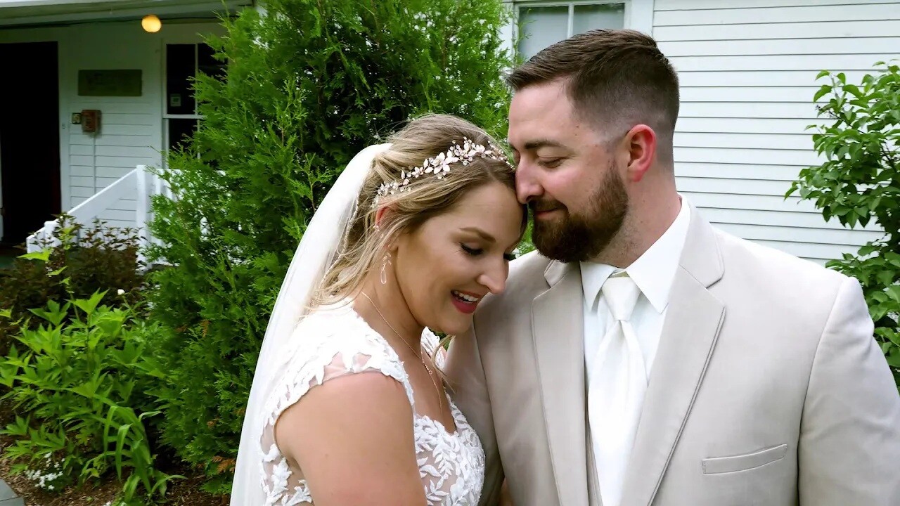 Bride and groom embracing outdoors in front of a residential home with lush green foliage