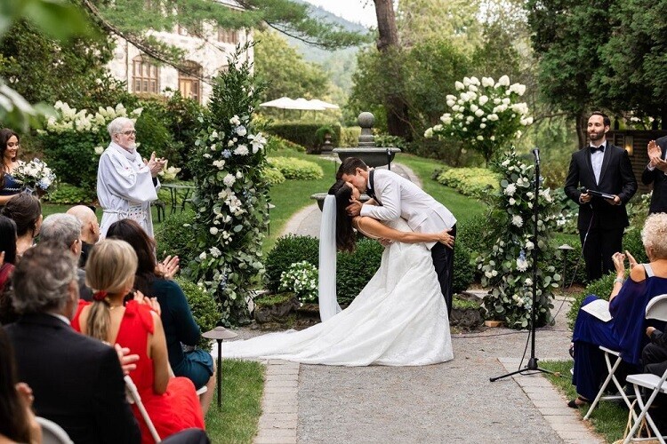 Bride and groom kissing at outdoor garden wedding ceremony with floral arch