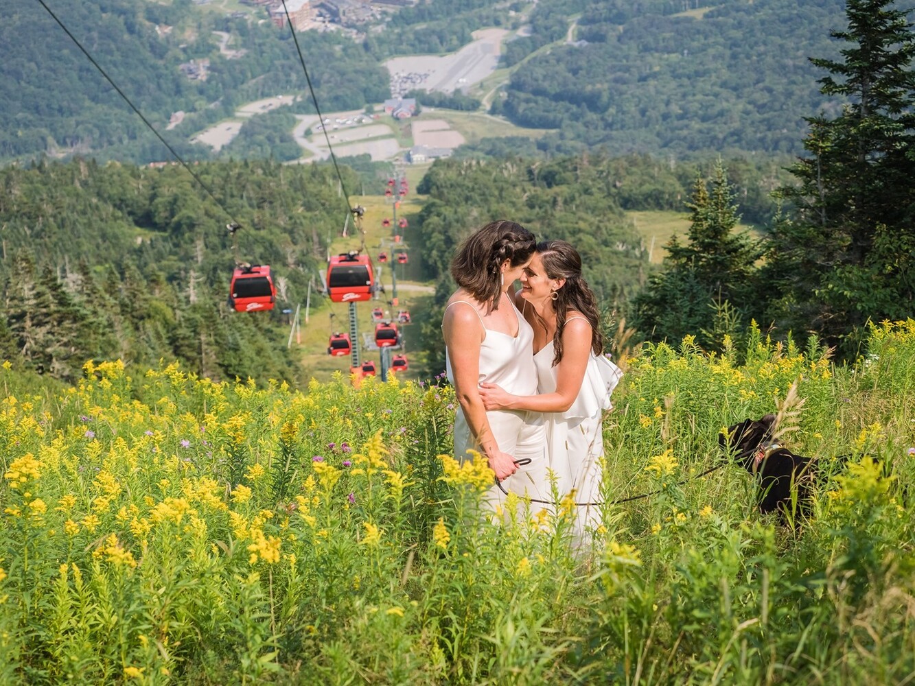 Woman in white dress posing in alpine meadow with gondola lift and valley landscape