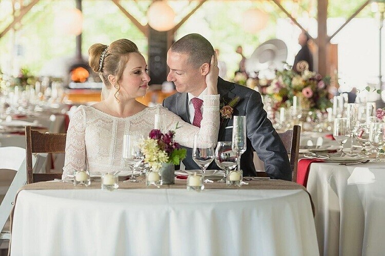 Bride and groom seated at sweetheart table during reception, exchanging glances