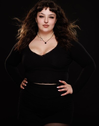 Woman with long wavy dark hair wearing black velvet crop top against black background