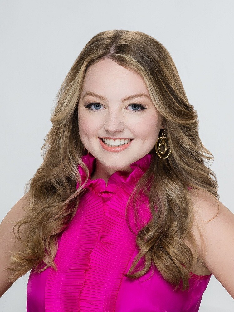 Woman with long wavy brown hair smiling at camera wearing bright magenta sleeveless top