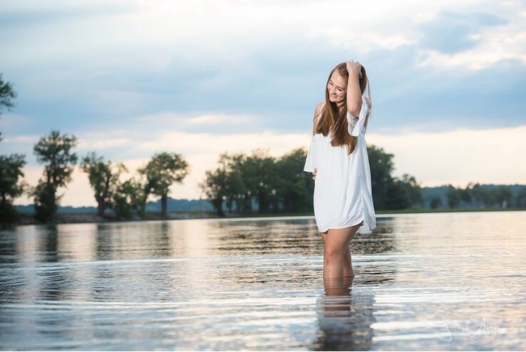 Young woman in white shirt standing in shallow lake water with hand to head