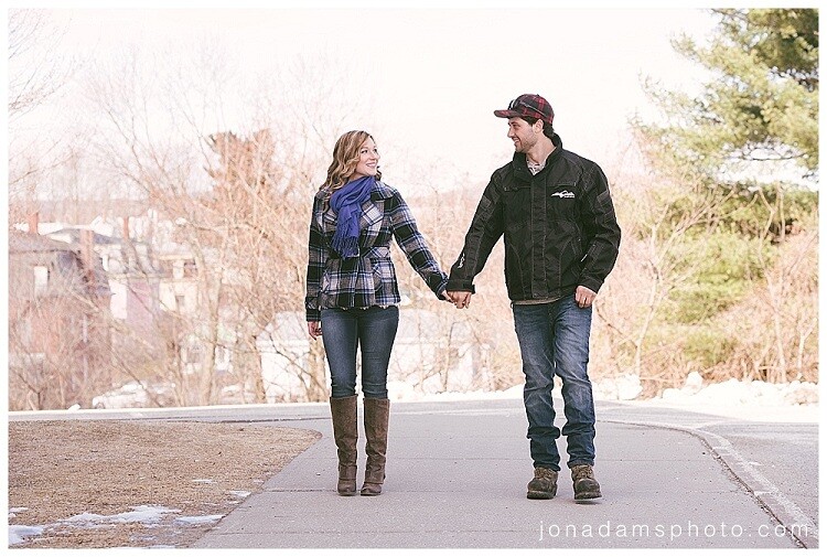 Couple holding hands walking down a paved road lined with bare and evergreen trees