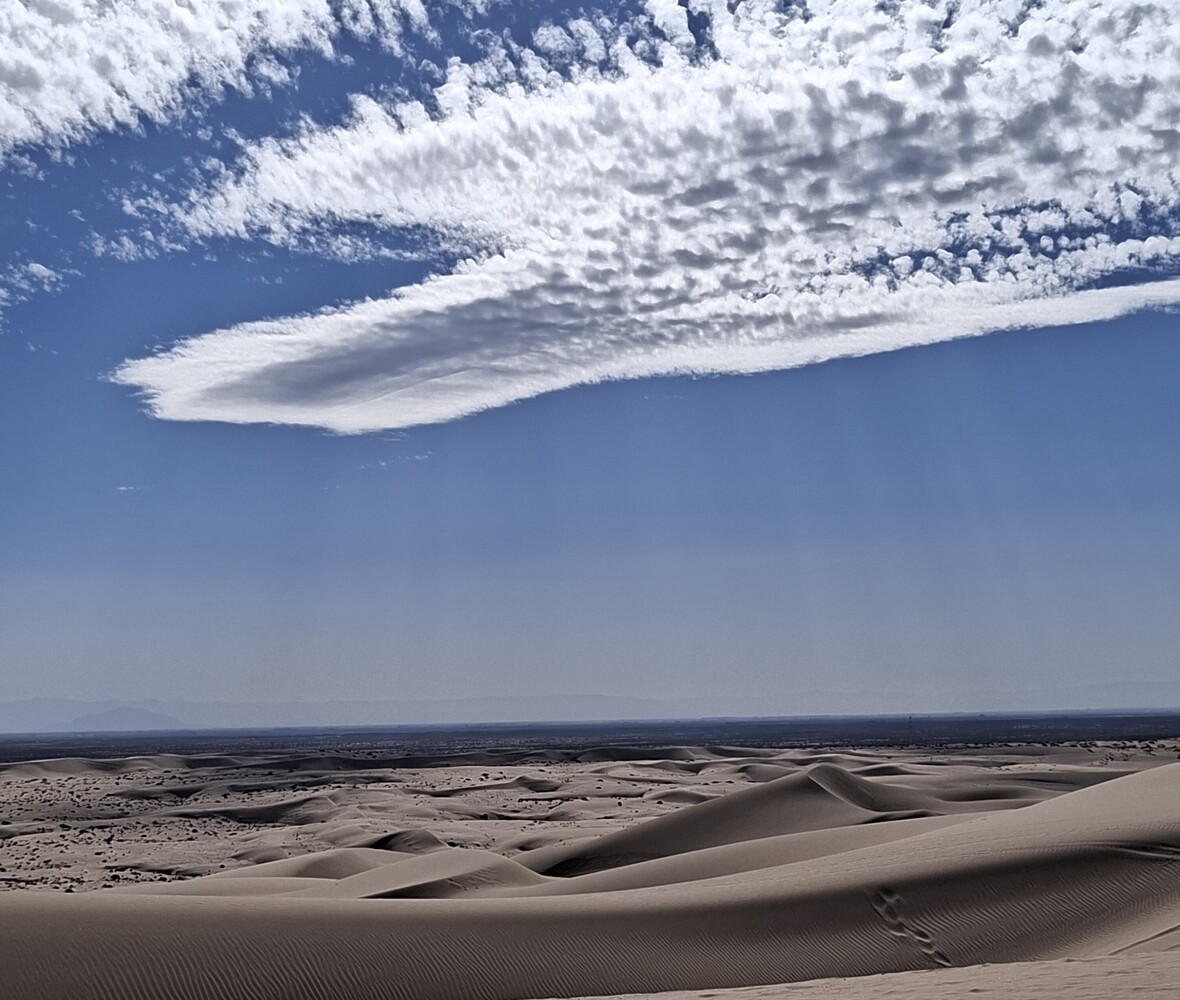 Desert dunes beneath dramatic lenticular cloud formation against blue sky