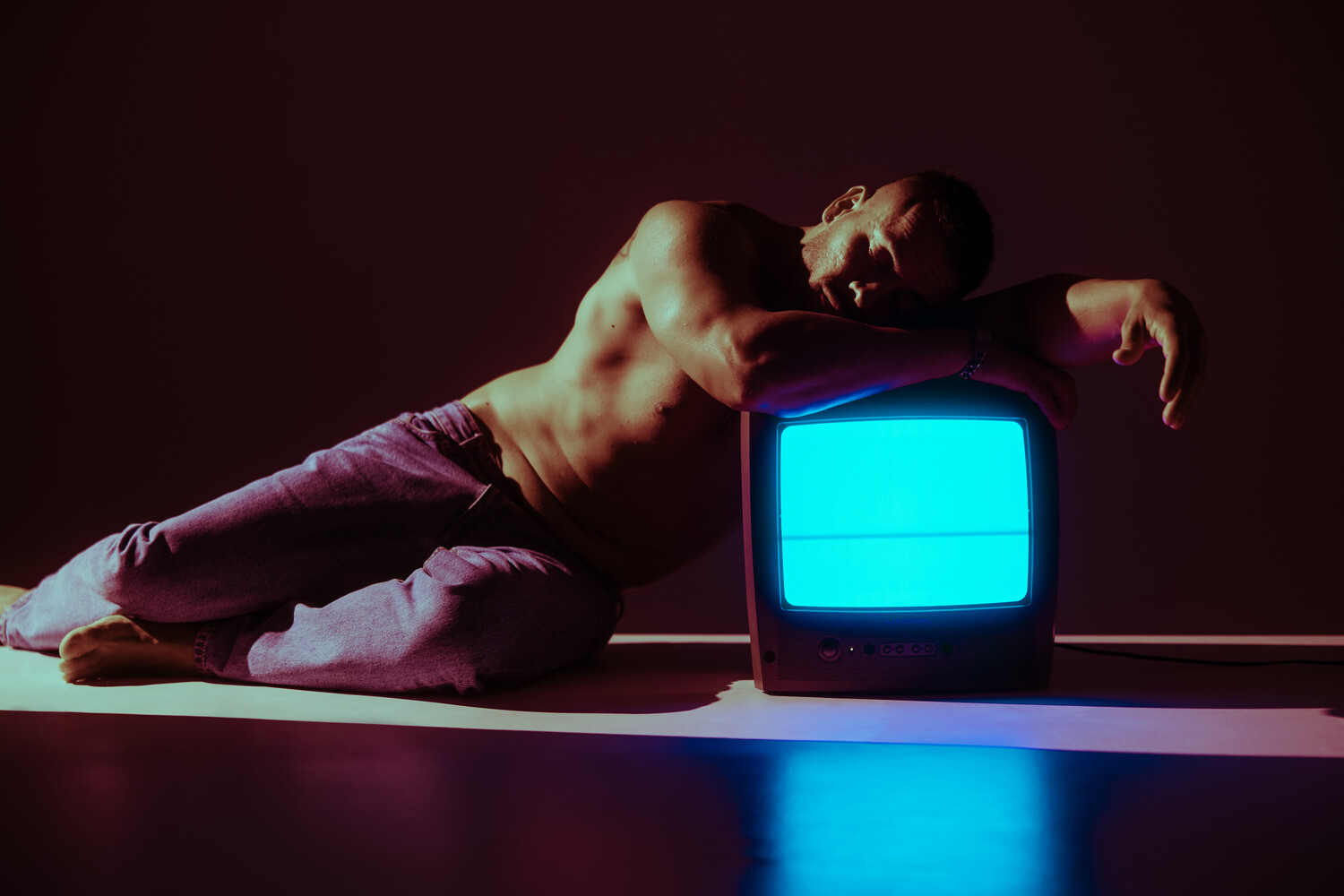 Shirtless person in pink pants leaning over a vintage CRT television with cyan screen