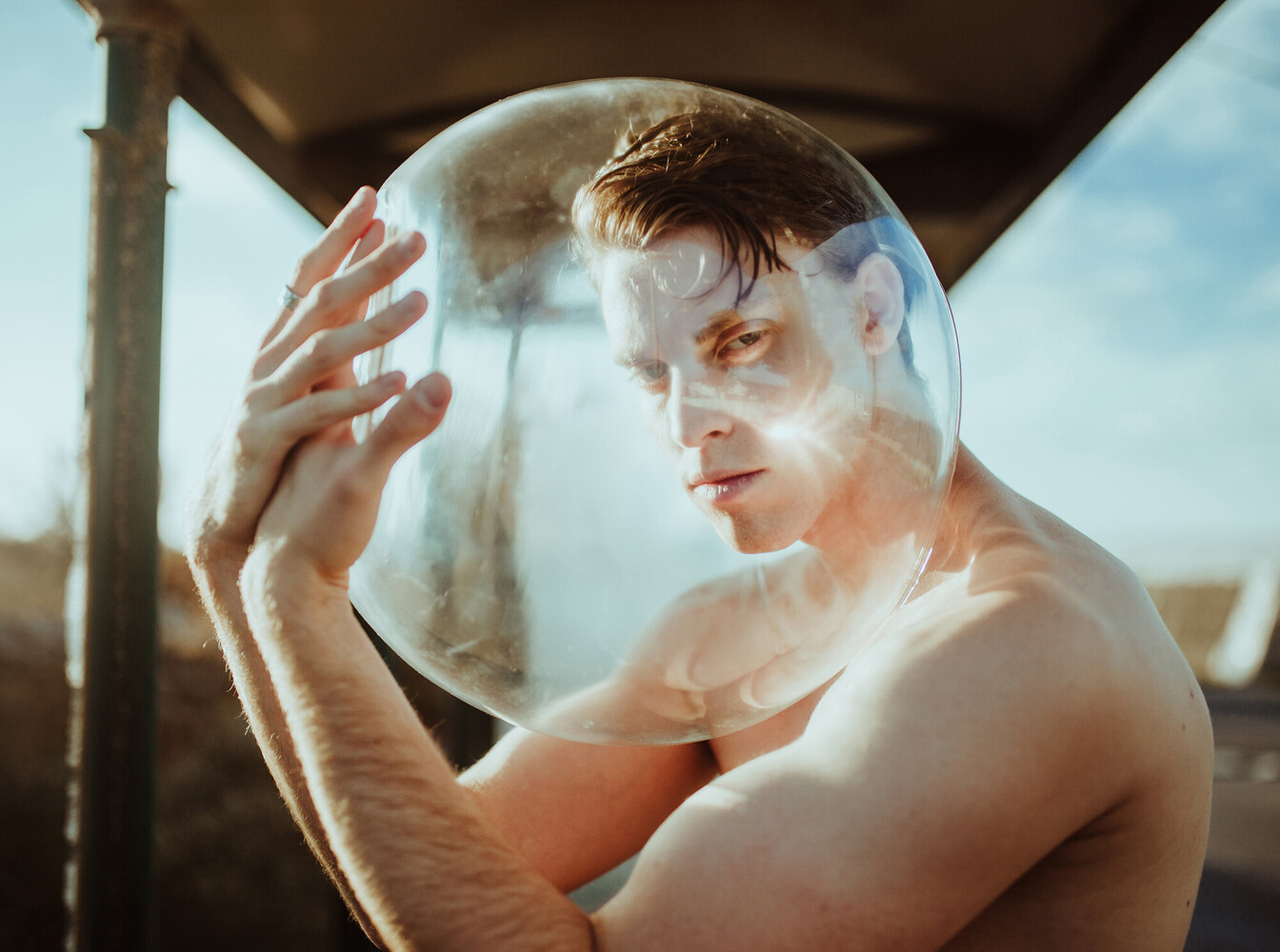 Shirtless man holding a large translucent sphere with his reflection visible inside it