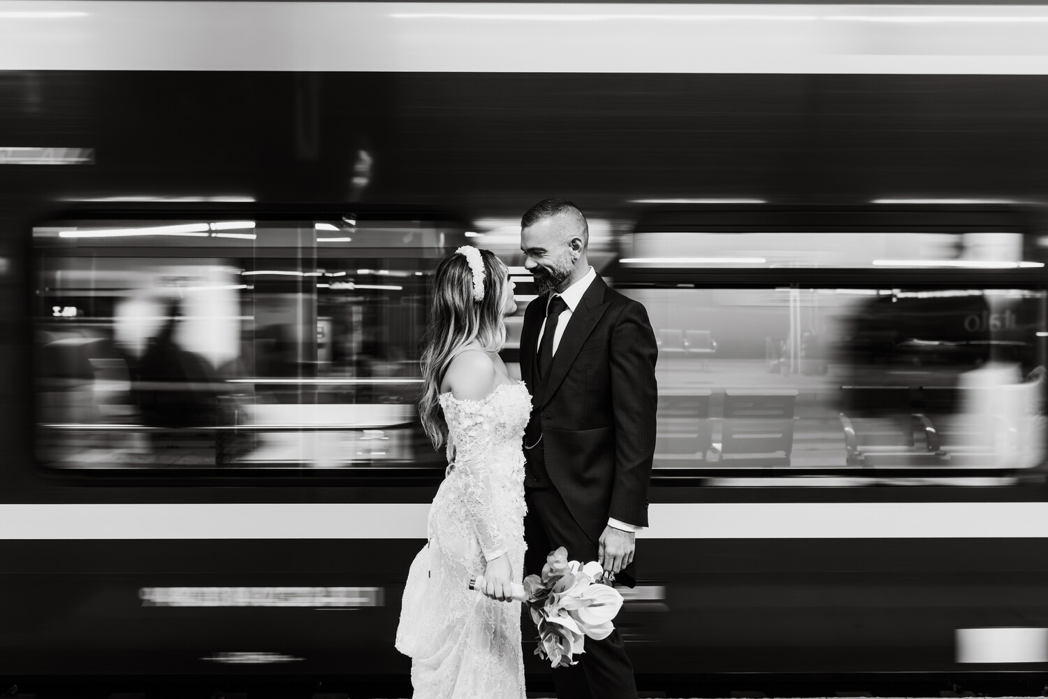 Bride and groom standing together with motion blur from passing vehicle behind them