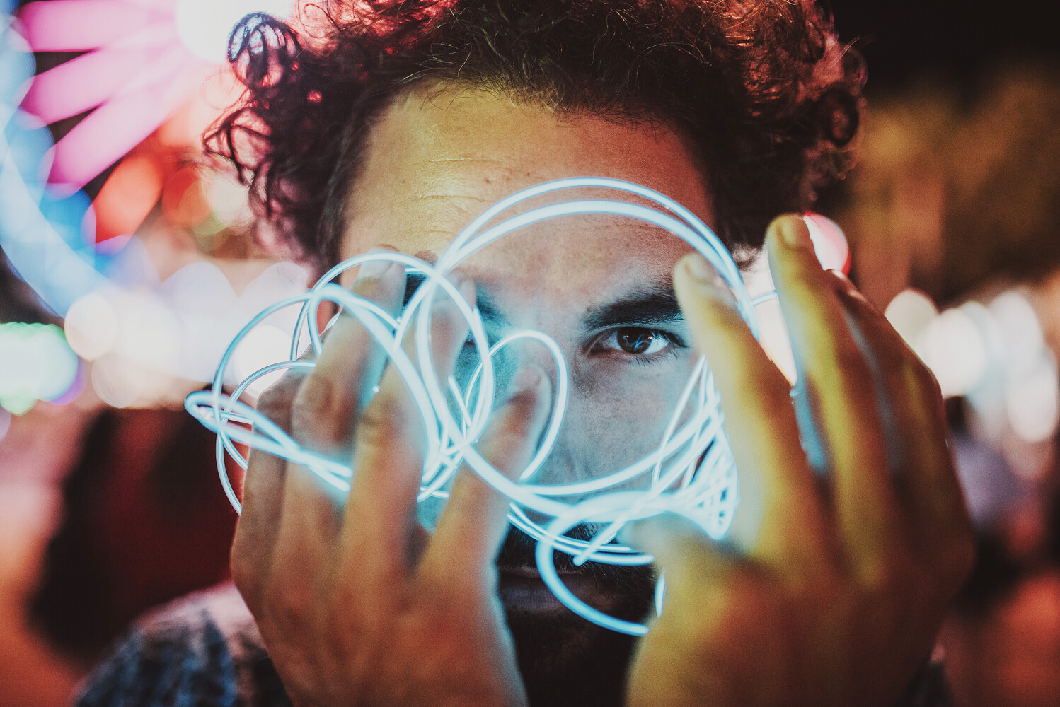 Person holding glowing neon wire light sculpture in front of face