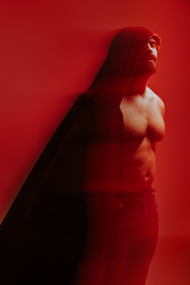 Shirtless male figure in profile against vibrant red background with dramatic shadow