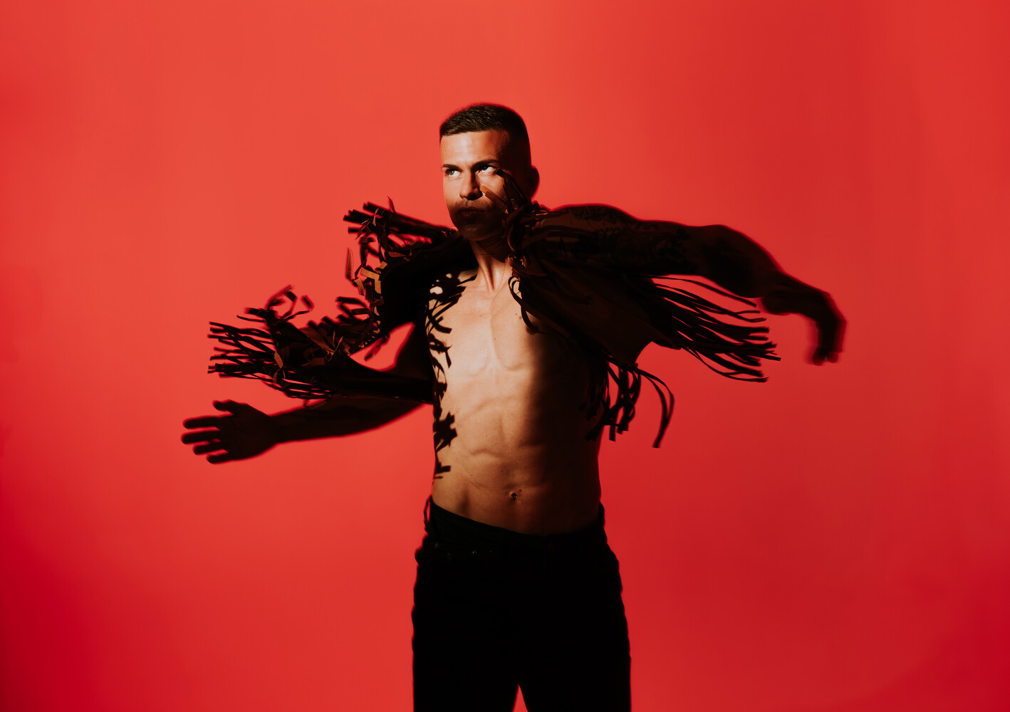 Shirtless man with arms outstretched against vibrant red background