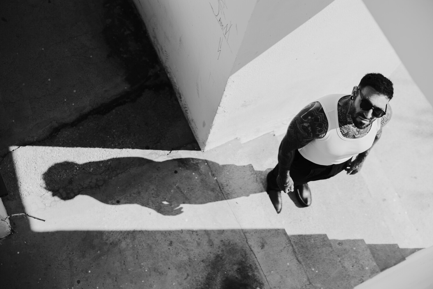 Man in sunglasses and dark jacket viewed from above against geometric black and white floor.