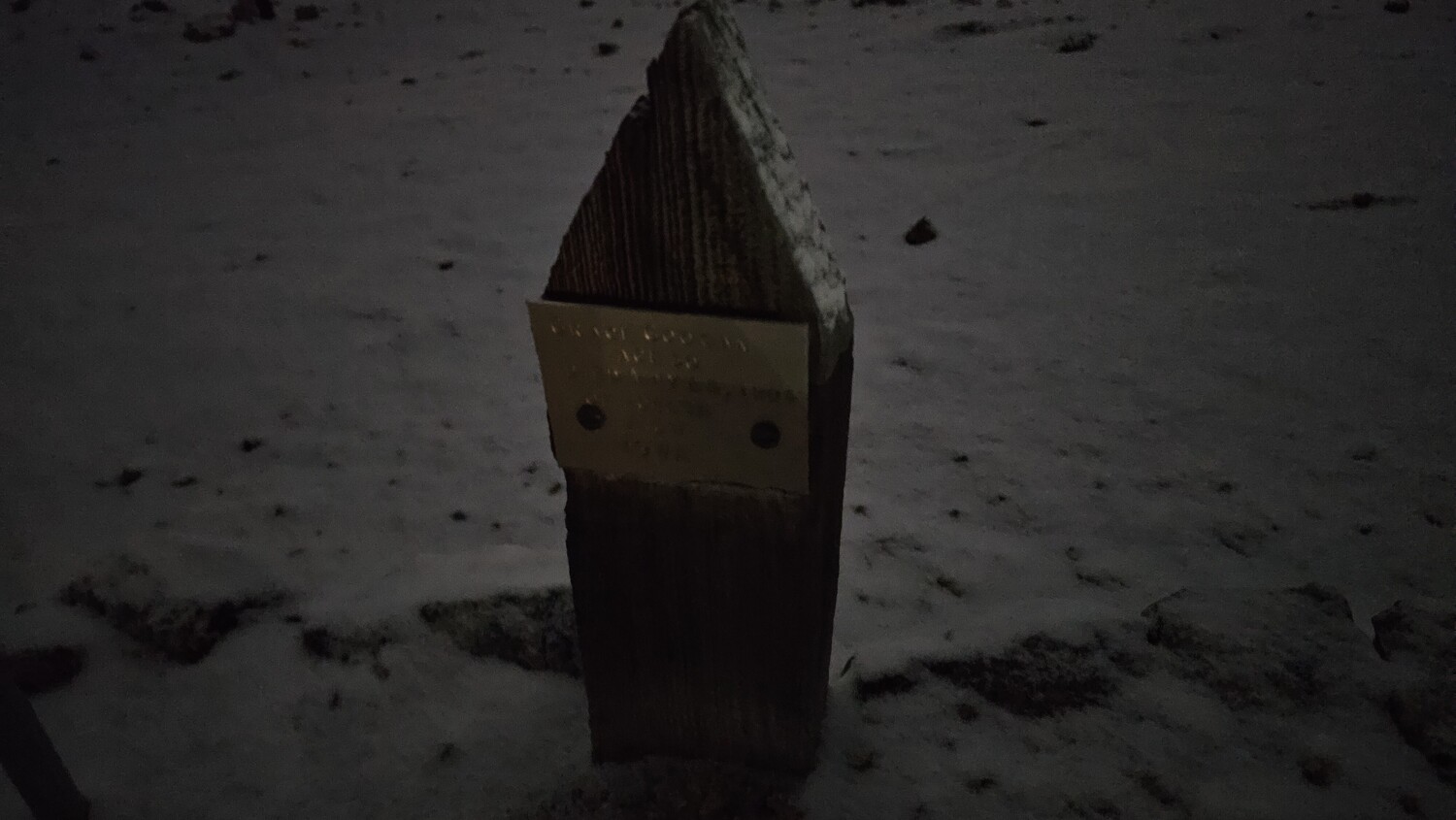 Wooden post with metal band sitting on snowy ground in dim lighting