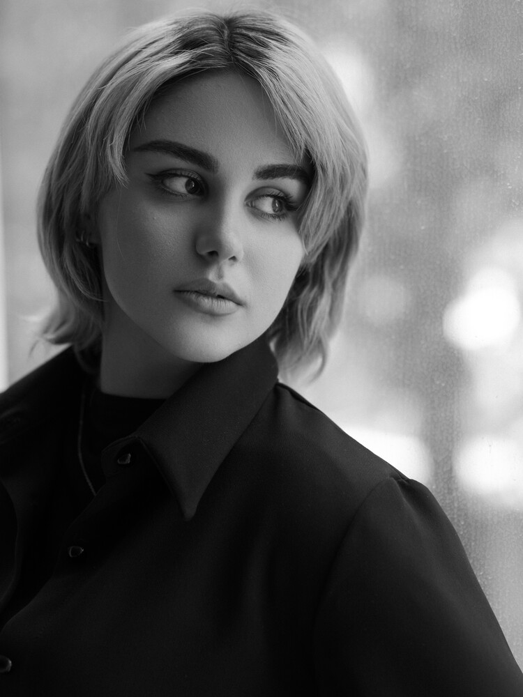 Portrait of a woman with short blonde hair wearing a dark collared shirt against a blurred background