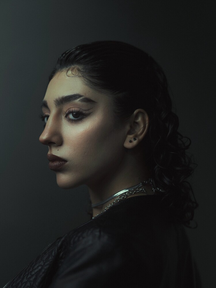 Woman in profile with dark hair and metallic collar against dark background