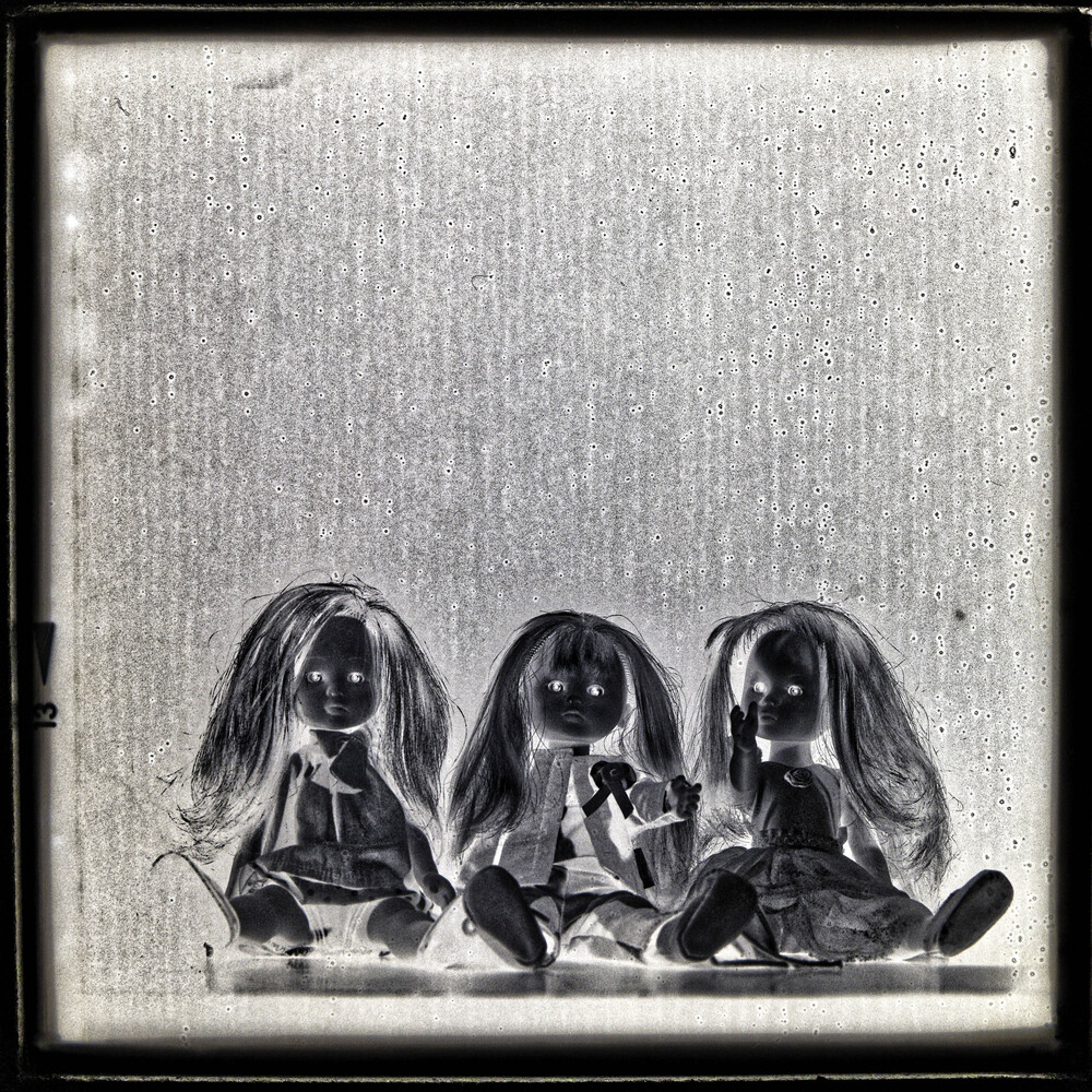 Three dolls with long hair seated side by side in a black and white photograph
