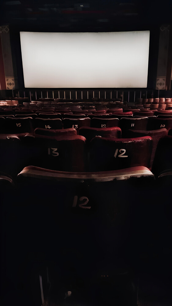 Empty cinema auditorium with blank projection screen and red seats