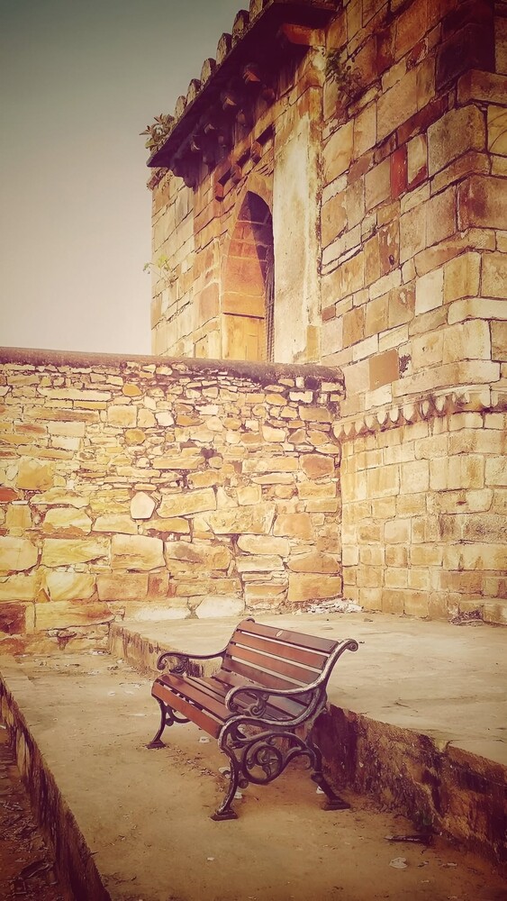 Wooden bench on sandy ground against weathered golden stone architecture