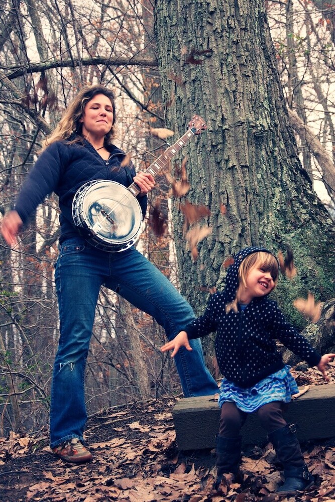 Two people posing with vintage cookware against a large tree in autumn woods
