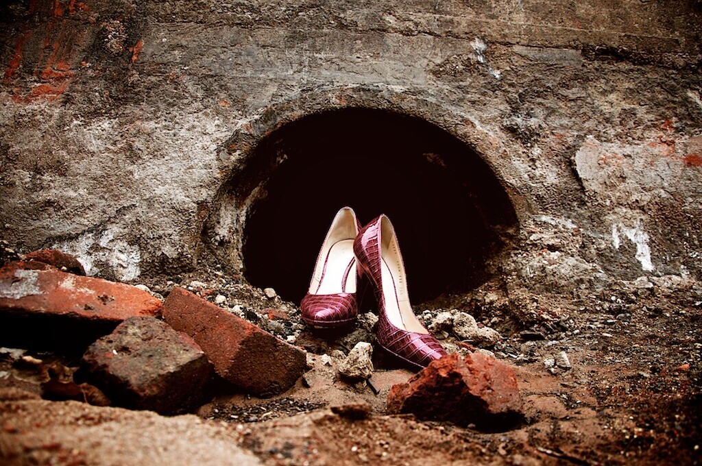 Pair of burgundy heels positioned in a dark circular opening in a weathered concrete wall
