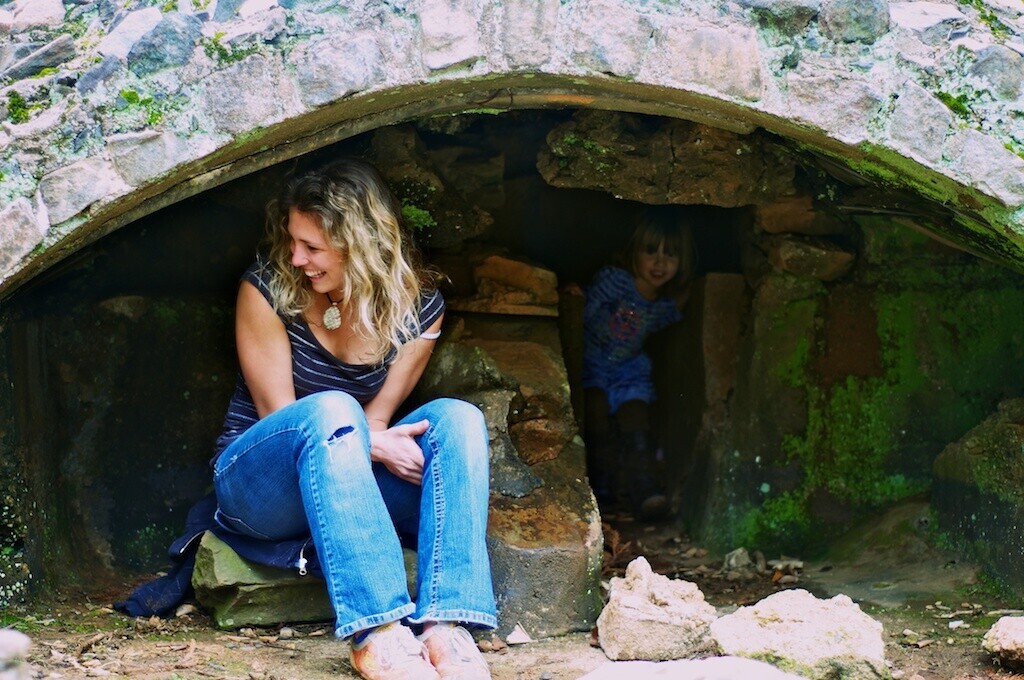 Woman sitting at entrance of moss-covered stone tunnel or archway