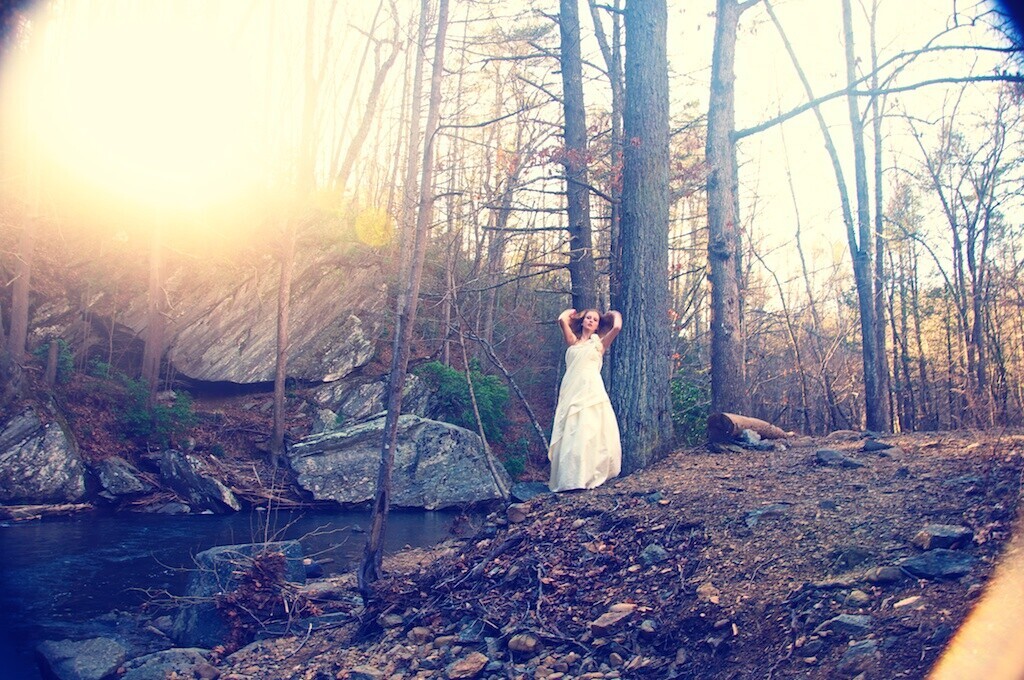 Woman in white dress standing by a stream in bare winter forest at golden hour