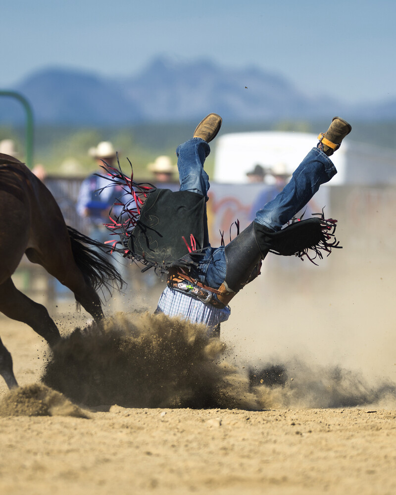 Rodeo rider airborne after being thrown from a bucking horse in sandy arena