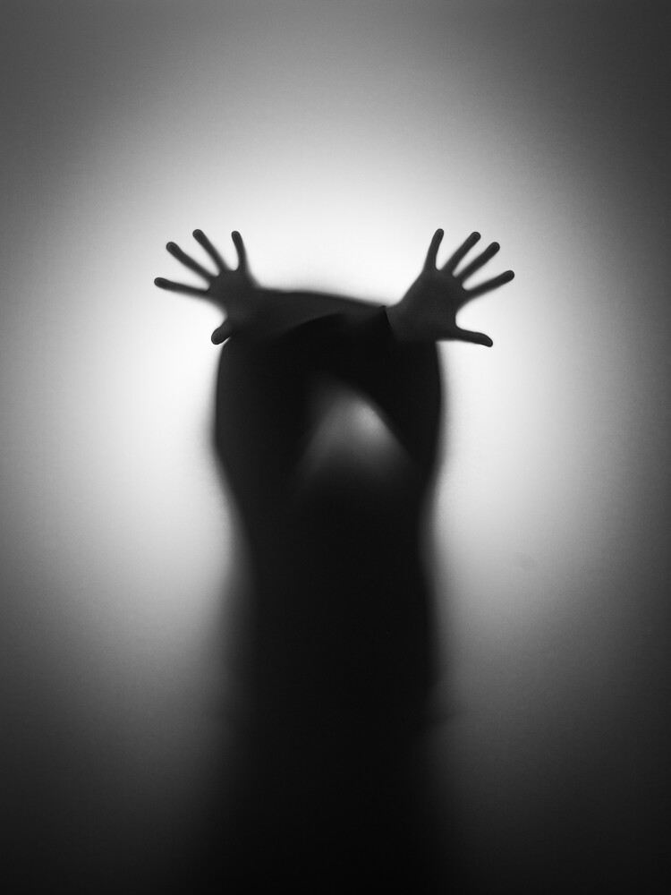 Blurred black silhouette of a figure with fingers spread, hands pressed against a glowing translucent screen.