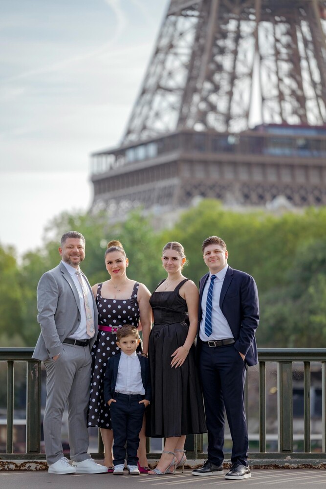 Family of five posing in front of the Eiffel Tower on a Paris riverside bridge in soft daylight