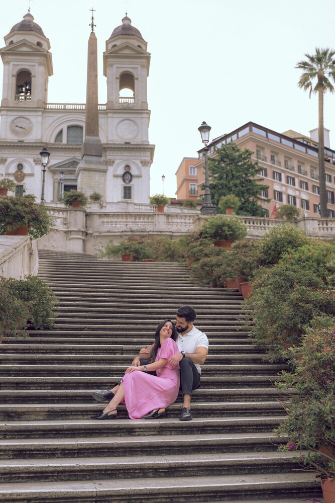 Couple embracing while seated on the Spanish Steps in Rome, with Trinità dei Monti church and obelisk behind them.