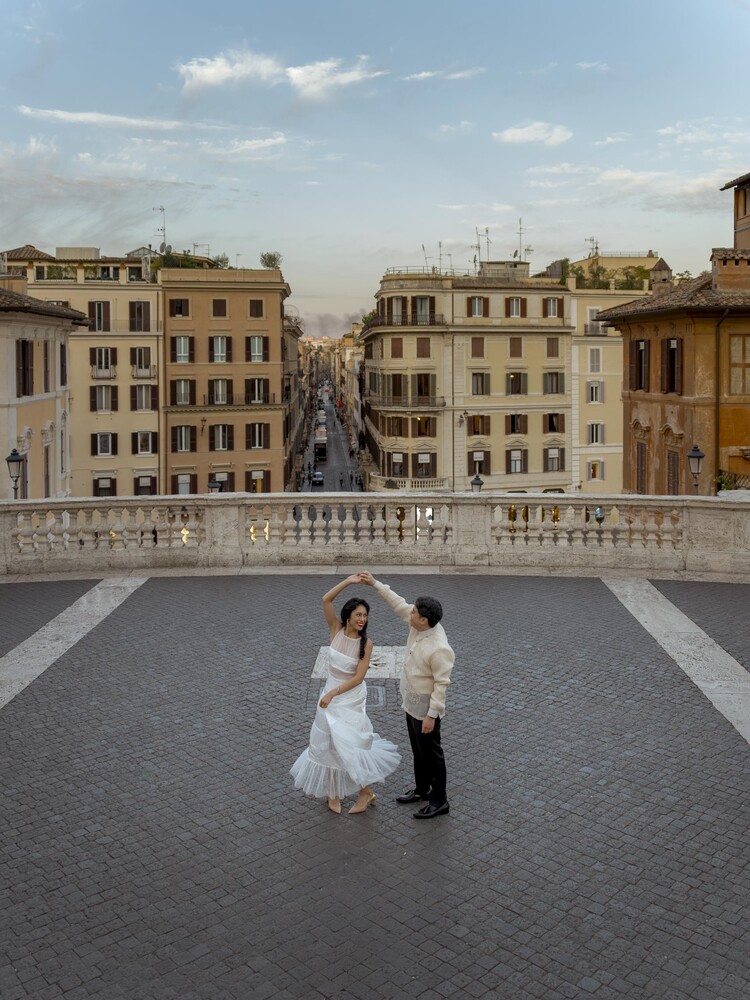 Couple dancing on a stone terrace above a historic European street lined with ochre and cream buildings