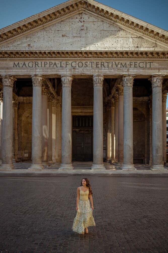 Woman in a flowing floral dress standing before the columned facade of the Pantheon in Rome.