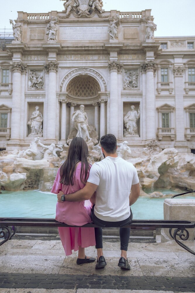 Couple seated on a railing with their backs to the camera, facing the ornate Trevi Fountain in Rome