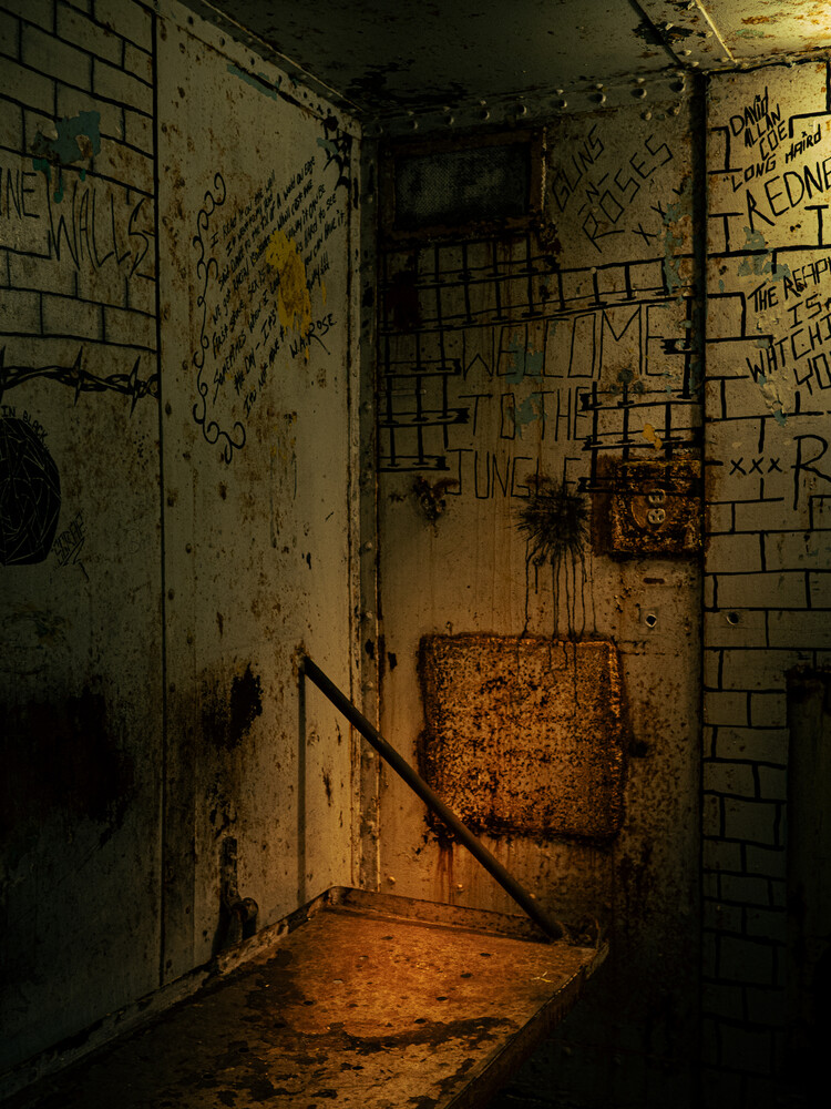 Graffiti-covered tiled corner of an abandoned room with a rusted metal panel and warm light pooling on the grimy floor