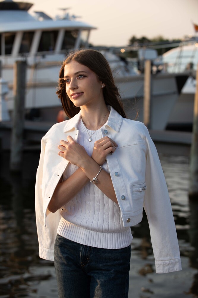 Woman in white blazer and knit sweater posed at marina with boats in background